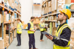 Focused warehouse manager writing on clipboard in a large warehouse